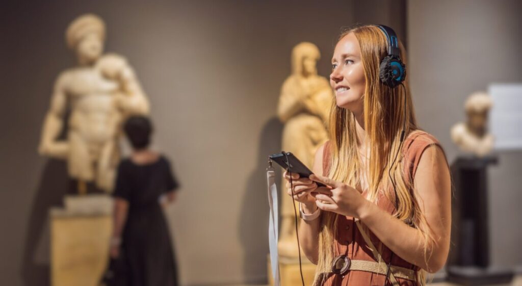 A young woman looking at sculptures and listening to an audio guide.