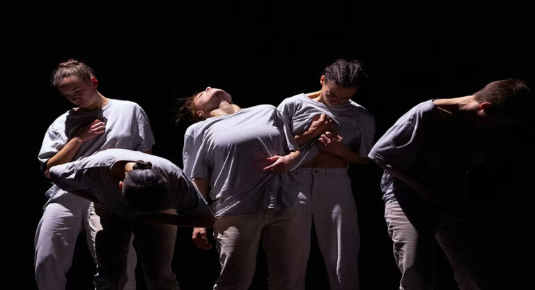 Dancers in gray against black background.