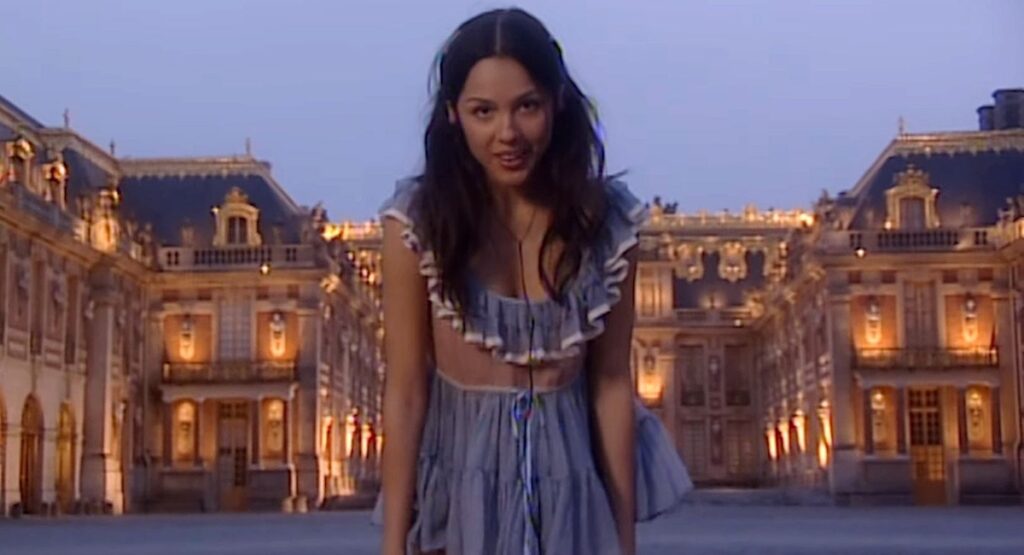 Olivia Rodrigo standing in front of the Palace of Versailles.