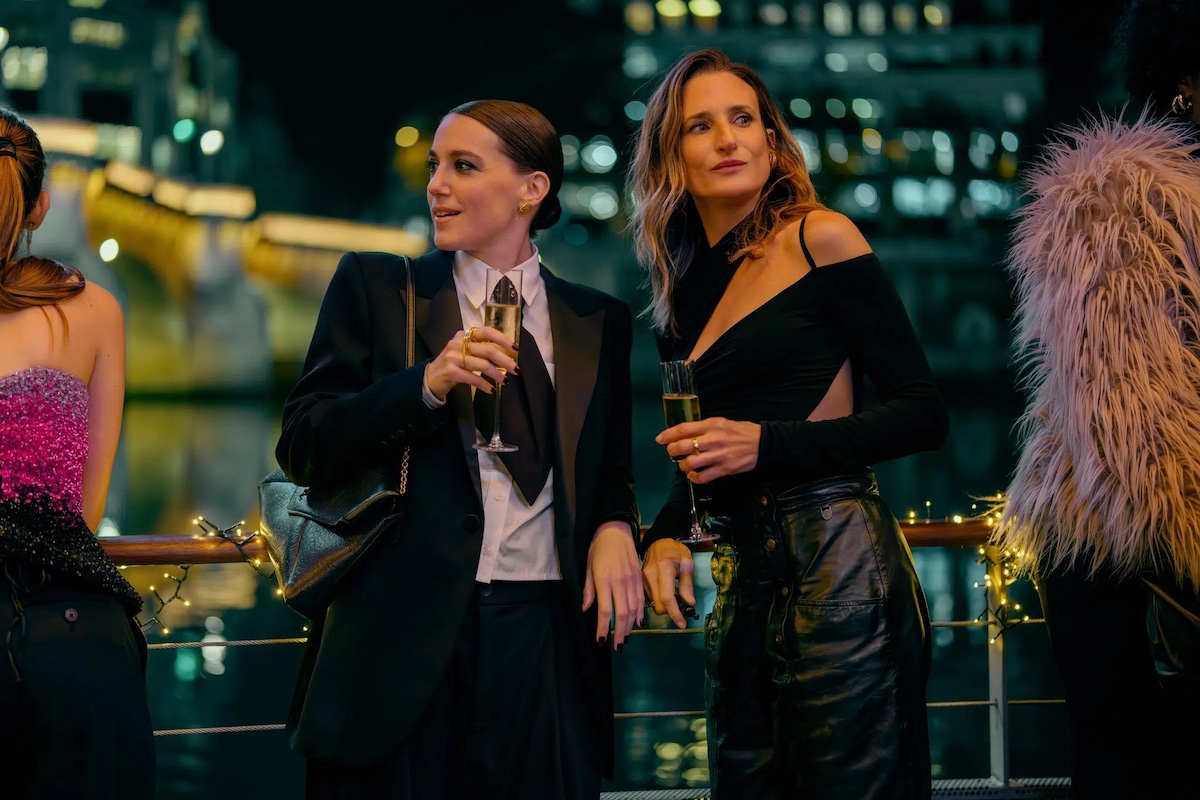 Two women in chic attire drinking on rooftop.
