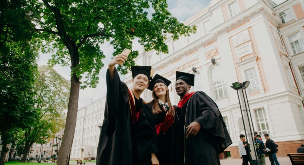 Some students are taking pictures of themselves for their diploma in front of their university.