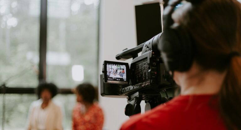 Person holding film camera while filming two women in distance.