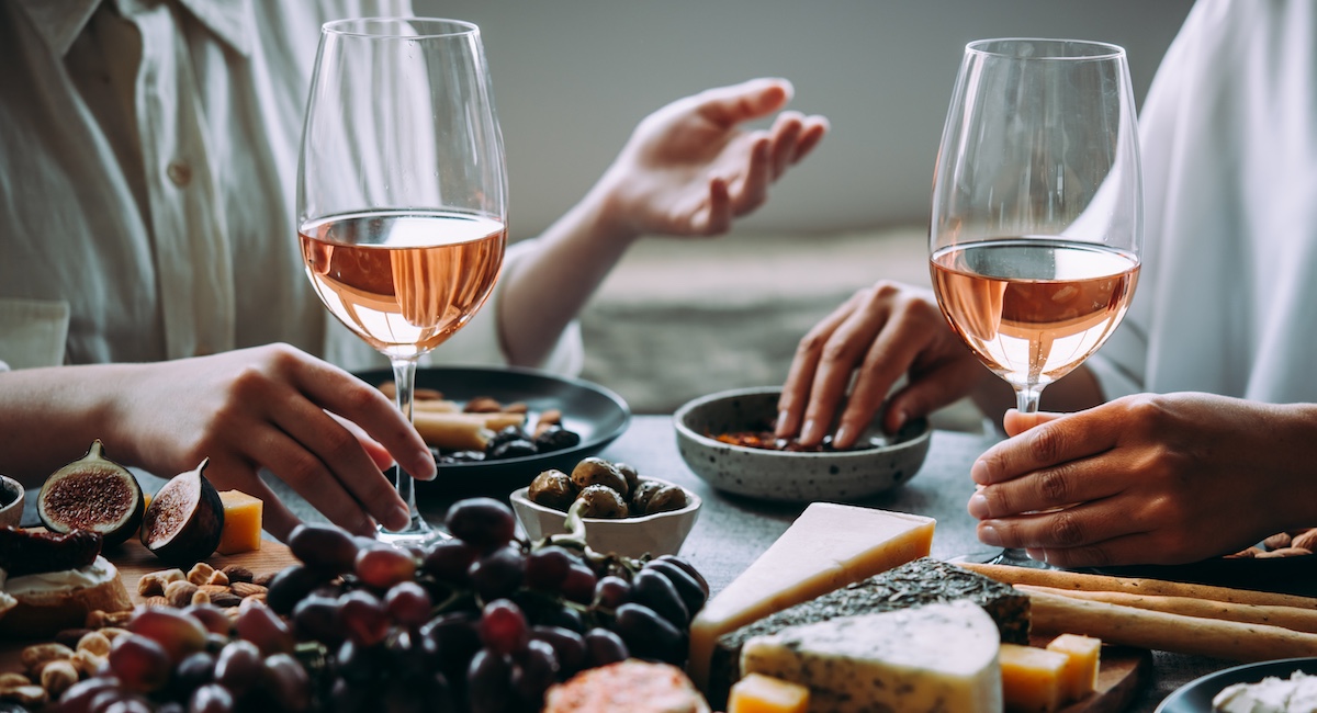 Two people drinking wine while snacking on cheese board.