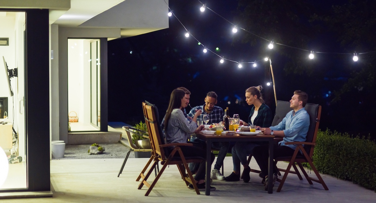 People eating on a back patio with lights strung up at night.
