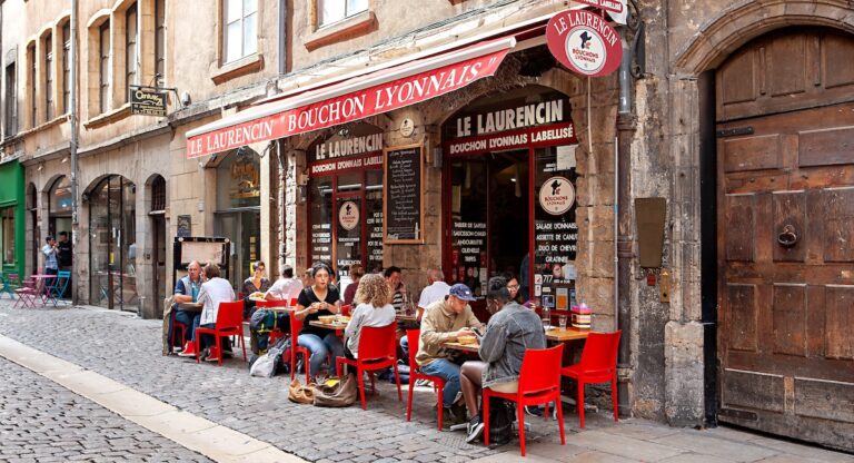 Exterior of a Bouchon restaurant in Lyon, with people seated at tables on the terrace.