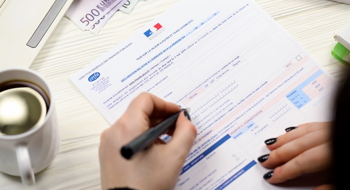 Accountant fills out French tax form with coffee beside her on table.