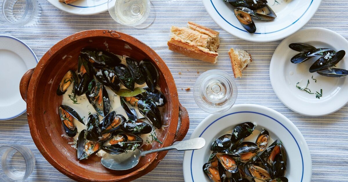 Moules marinieres, bread, and white wine on table