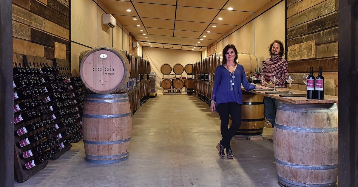 Man and woman standing by barrels in winemaking facility