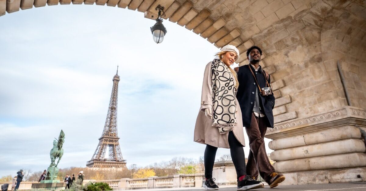 Couple walking under bridge by Eiffel Tower.