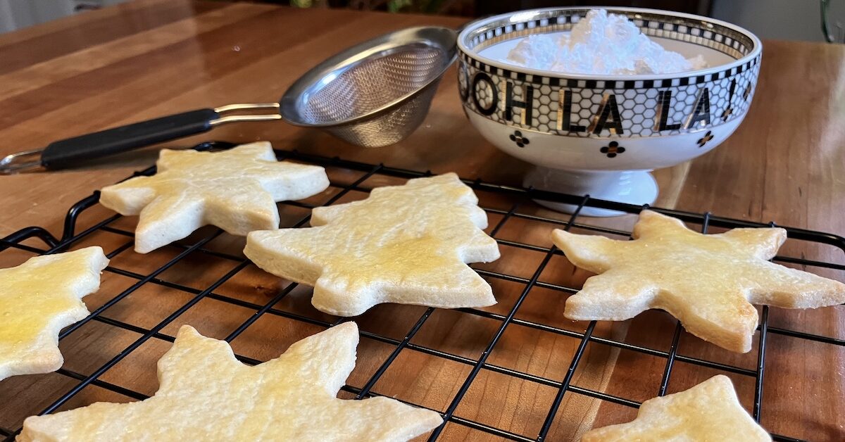 Cutout Christmas cookies on cooling rack with bowl of powdered sugar