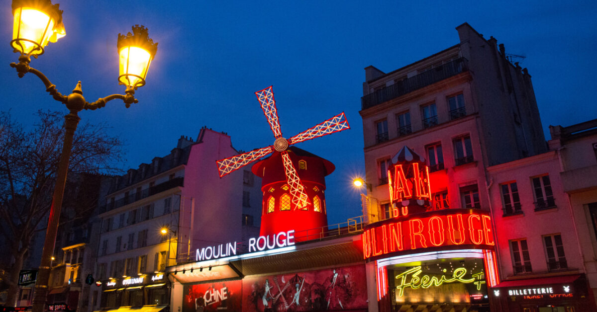 A store front at night with Moulin Rouge in the background