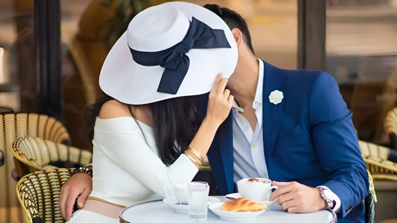 Man and woman with large hat kissing at cafe