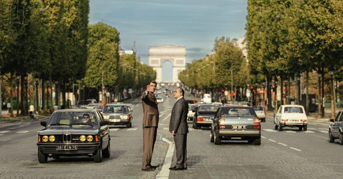 Two men standing in the middle of the Champs Elysees, with the Arc du Triomphe in the background