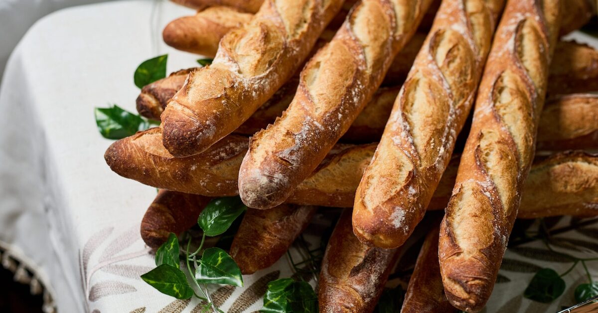 Bunch of baguettes piled neatly on table.