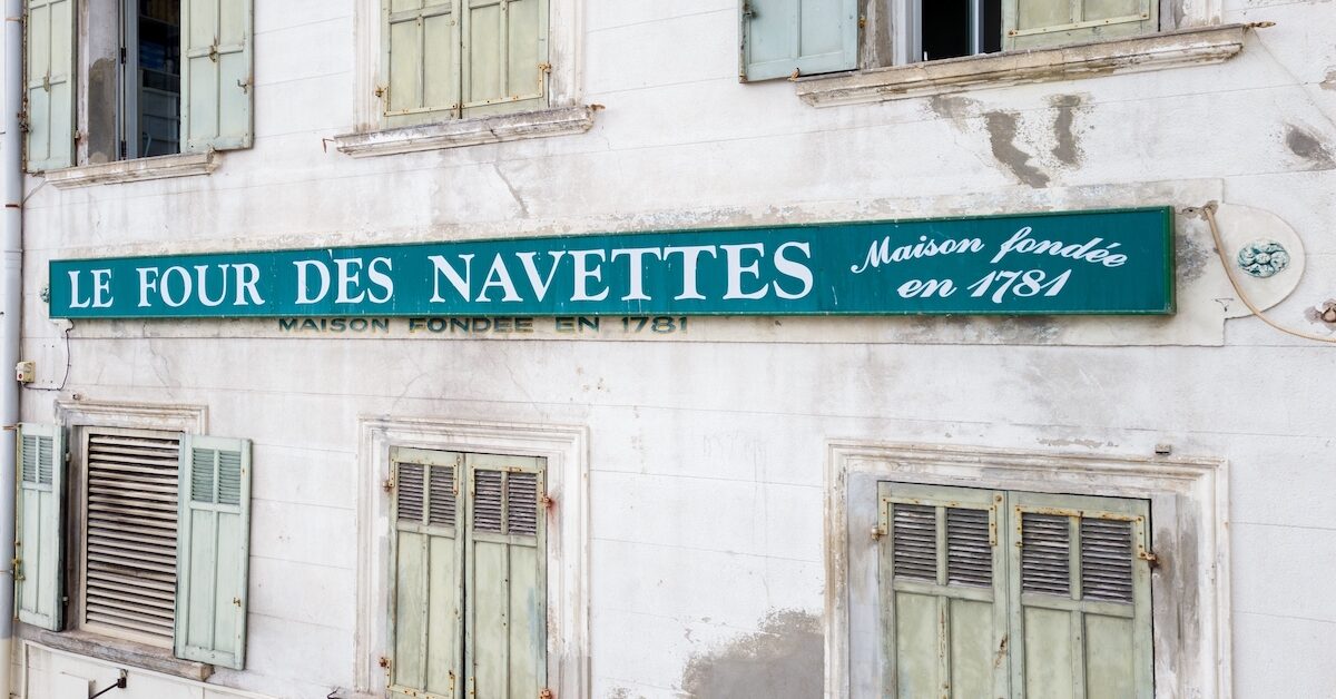 A green sign that reads "Four des Navettes, maison fondée en 1781" on the side of an old building in Marseille.
