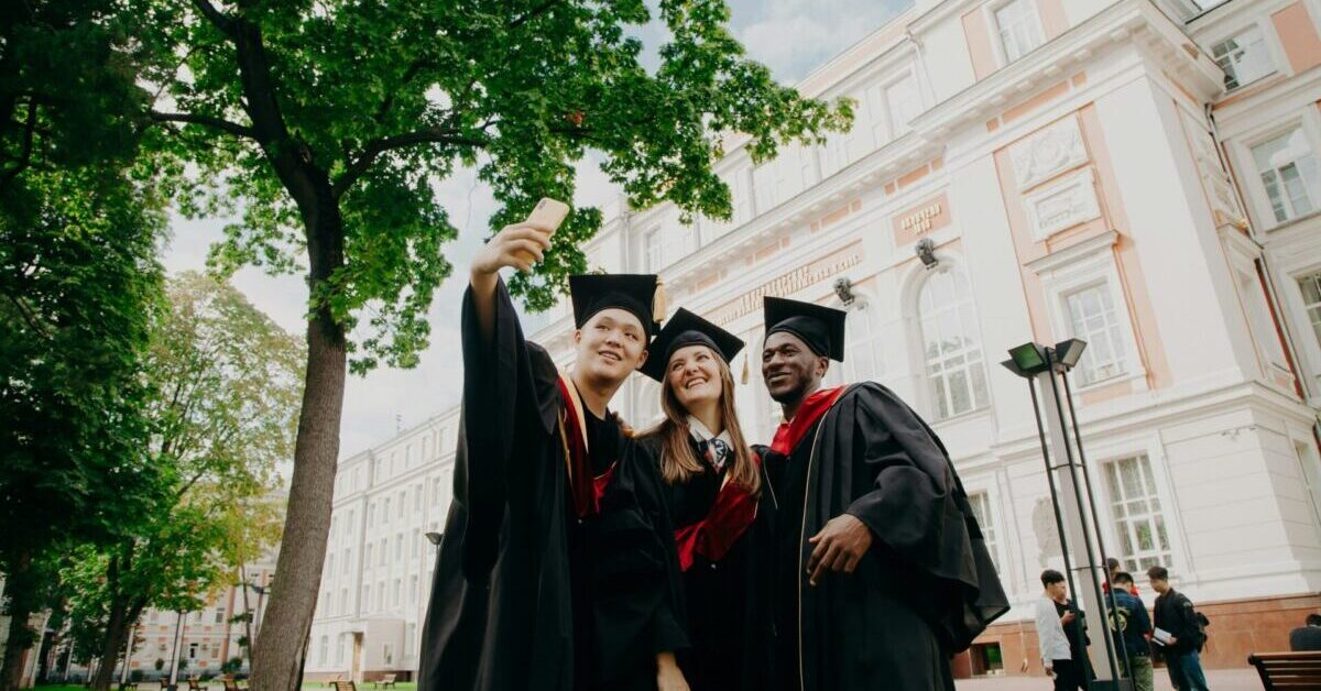 Some students are taking pictures of themselves for their diploma in front of their university.