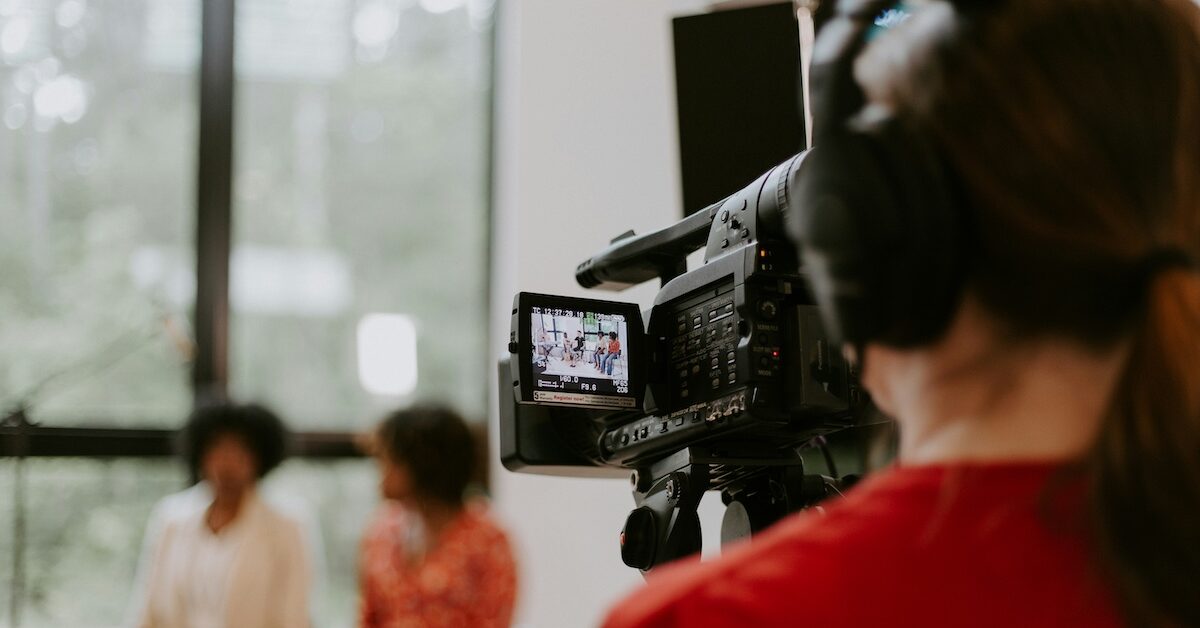 Person holding film camera while filming two women in distance.