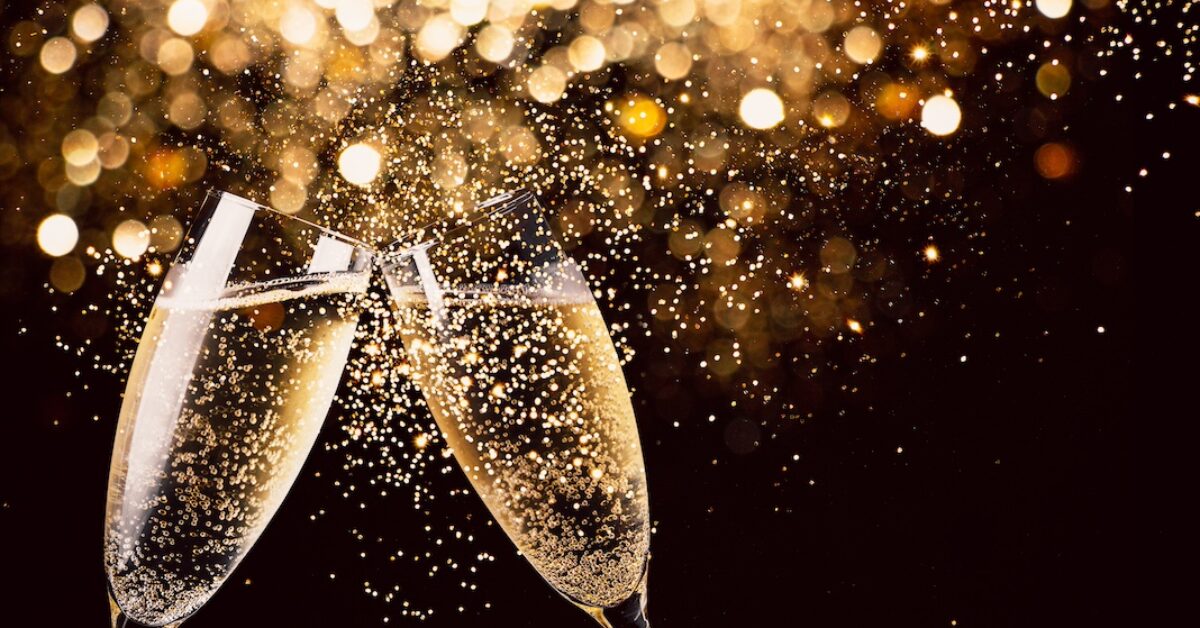 Two glasses of champagne toasting in the night with lights, glitter and sparks in the background