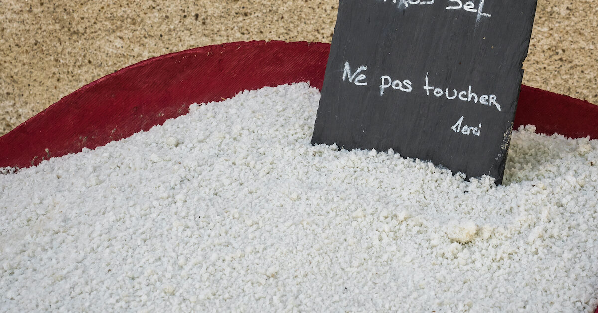 Red bin with gros sel (a coarse and unrefined grey sea salt) for sale in Guerande, France, with a handwritten sign that says “Ne pas toucher” (Do not touch).