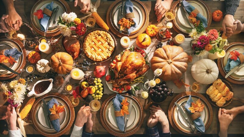 Group of friends or family members holding hands at festive turkey dinner table together. Thanksgiving celebration traditional dinner concept
