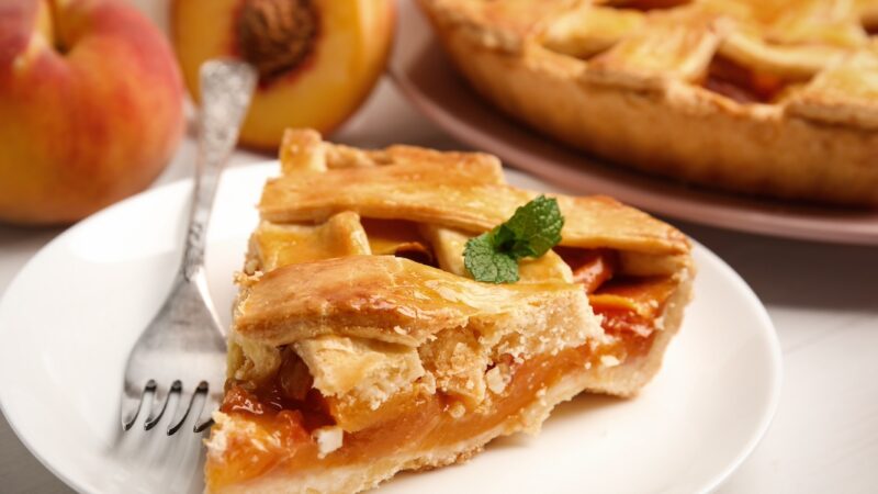 Piece of delicious fresh peach pie served on white table, closeup