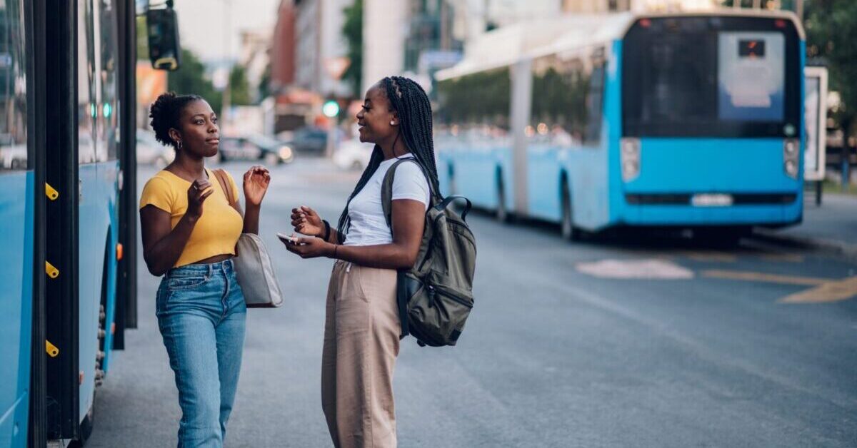 Two young women having a discussion at a bus stop.