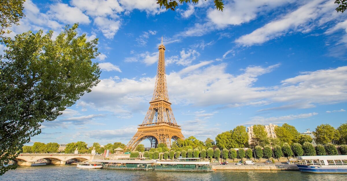 A panoramic view of the Eiffel Tower against a background of blue sky and beautiful clouds and the Seine River on a sunny day in Paris.
