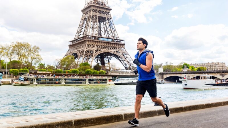 Man training and doing fitness exercises along the Seine river in Paris with Eiffel tower on background - Multiracial young man enjoying sport on a sunny day