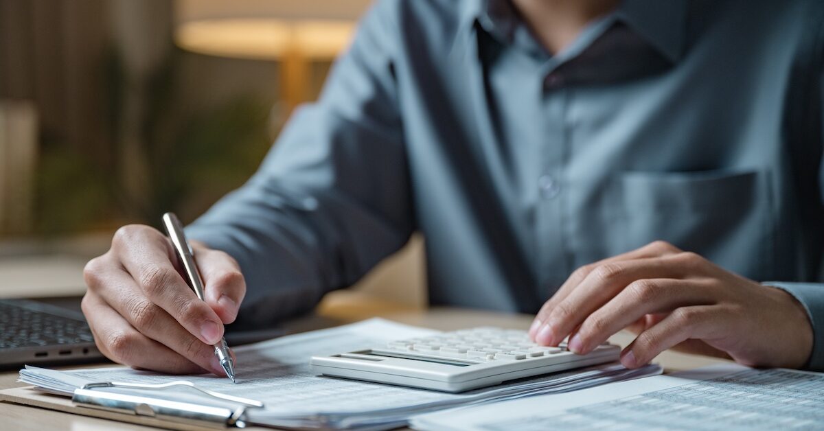 Man sitting at desk with calculator, filing taxes.