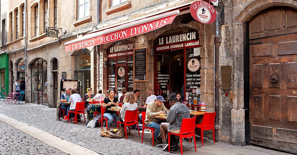 Exterior of a Bouchon restaurant in Lyon, with people seated at tables on the terrace.