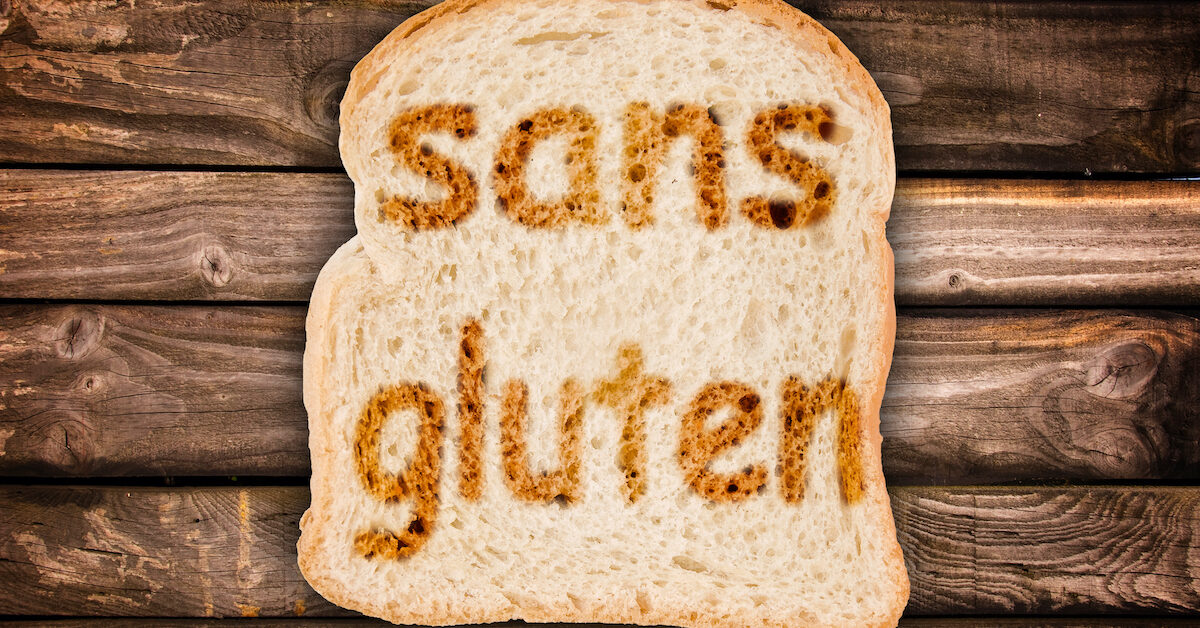 Text sans gluten (meaning gluten free in French) toasted on a slice of bread, isolated on wood background