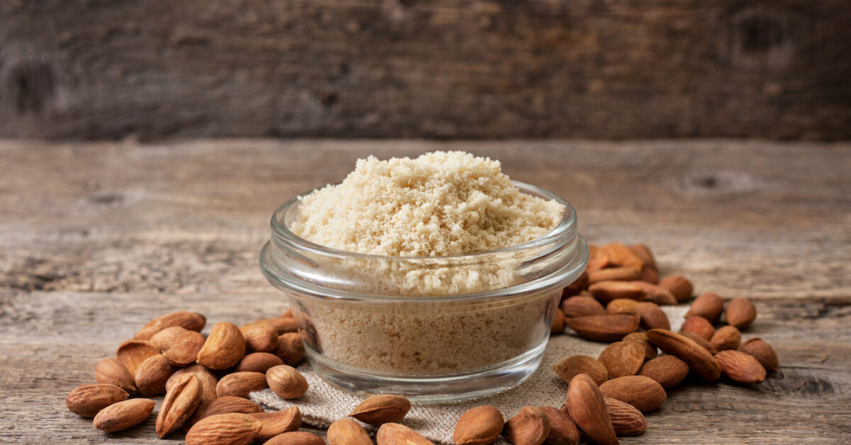 almond flour in a wooden bowl, almonds on old wooden background