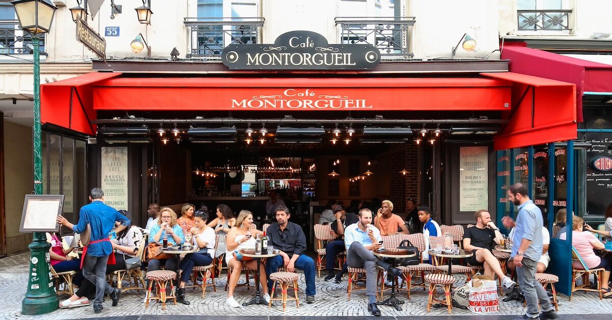 PARIS - AUGUST 23, 2017: People passes by a cafe on Rue Montorgueil street. People have brunch/lunch at cafe and enjoy nice weather on August 23, 2017.