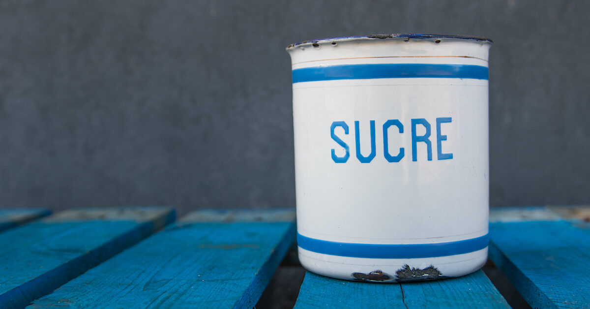 A vintage white bucket with sucre sugar written on it sitting on a blue picnic table.