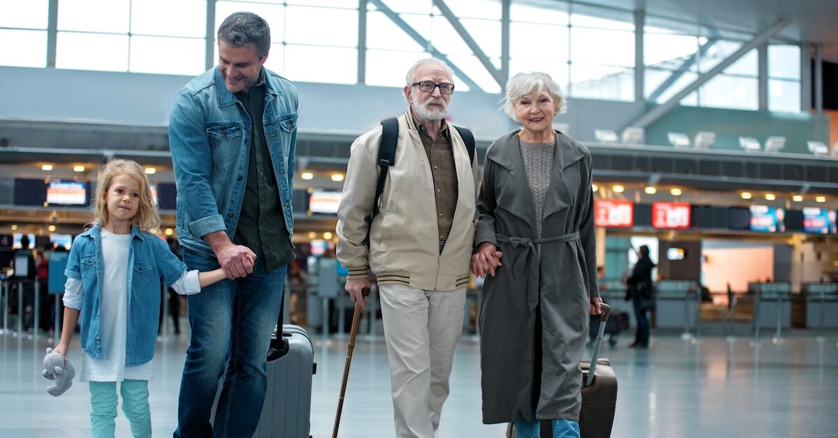 Full length of delighted old grandparents are going with their son and granddaughter at airport terminal to check-in on their flight.