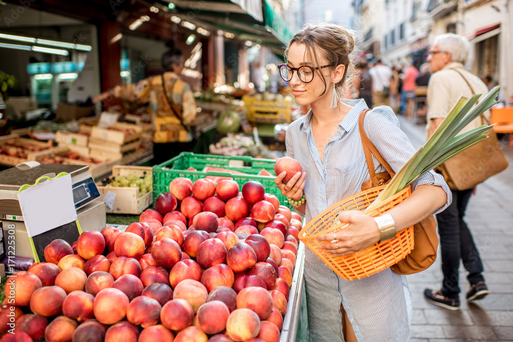 Young woman choosing a fresh peach standing with basket at the food market in France