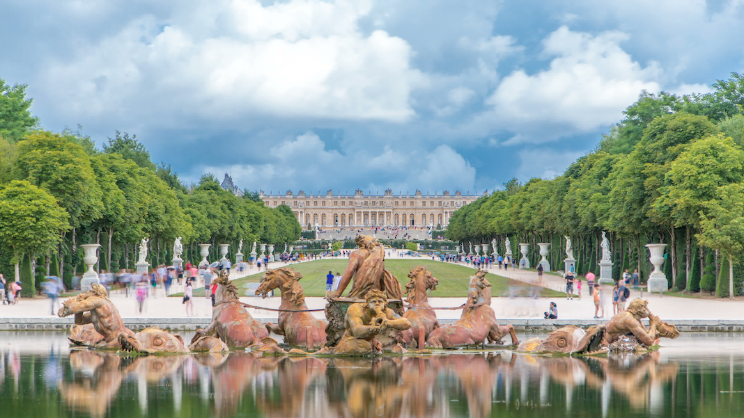 Apollo fountain in the Versailles Palace park, Ile de France. Royal Palace on background with reflection on water. Crowd of tourists at summer day